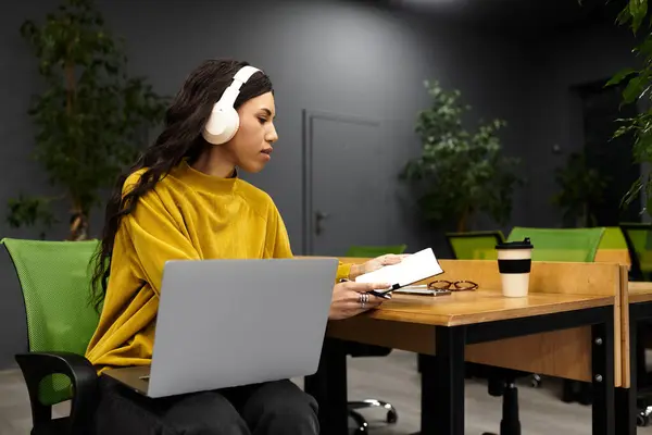 A beautiful young woman sits in a sleek office, engaged in her tasks while wearing headphones. — Stock Photo