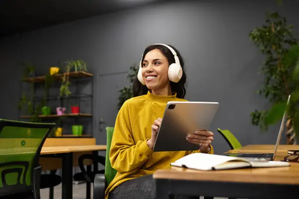 Smiling young woman in stylish attire engages with a tablet while seated in a lively office. — Stock Photo