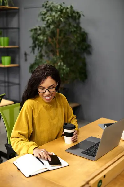 Elegante donna gode il suo caffè mentre lavora sul computer portatile in un ambiente elegante ufficio. — Foto stock