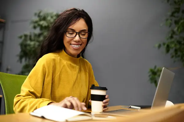 Una donna in bicchieri sorseggia caffè mentre lavora sul suo computer portatile e notebook. — Foto stock