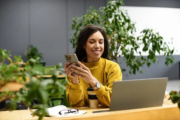 Joven profesional se involucra con su teléfono inteligente mientras está sentada en un entorno de oficina contemporáneo. - foto de stock