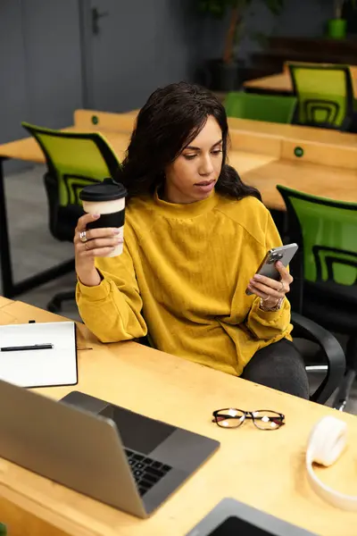 Stylishly dressed woman checks her phone with coffee in hand at a modern office. — Stock Photo
