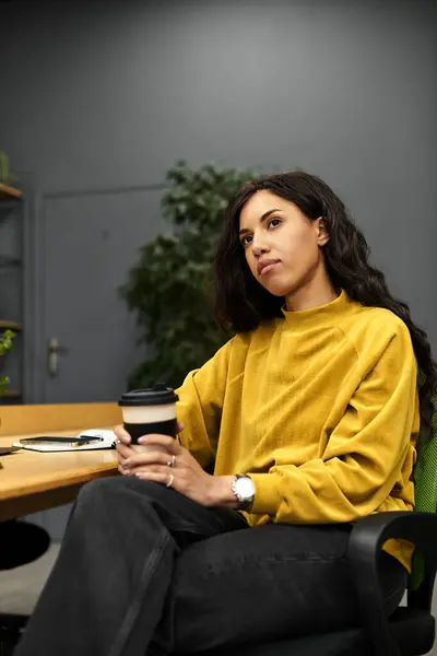 Young woman in modern office thoughtfully sipping coffee, showcasing elegance and focus. — Stock Photo