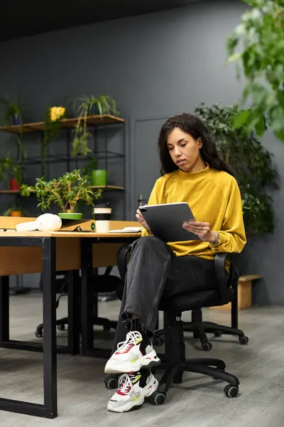 A beautiful woman sits at her desk in a stylish office, focused on her tablet amidst plants. — Stock Photo