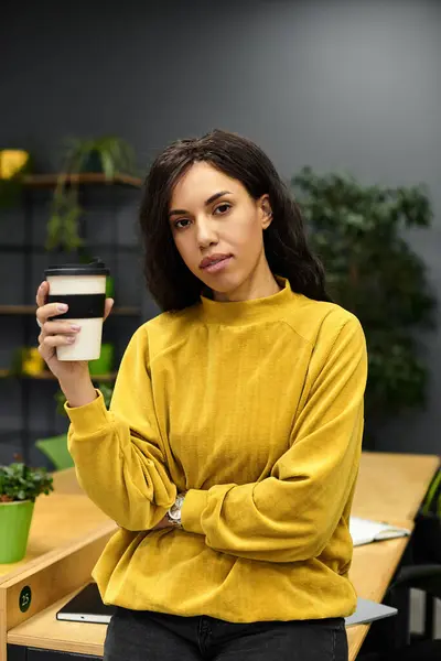 In a stylish office, a young woman stands with her coffee, exuding elegance and professionalism. — Stock Photo