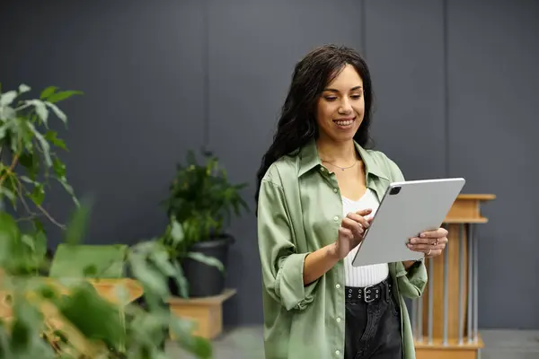 Woman smiles using a tablet in a stylish office with plants and modern decor. — Stock Photo