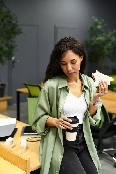 Bella donna prende un momento per assaporare il suo caffè e snack in uno spazio di lavoro contemporaneo. — Foto stock