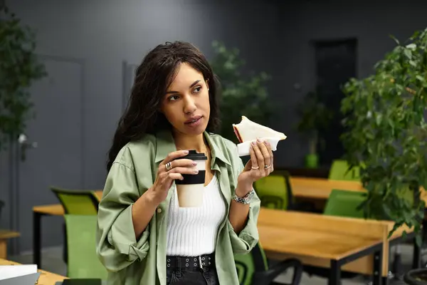 In a stylish office, a beautiful woman takes a moment to savor her meal and coffee during work. — Stock Photo
