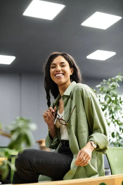 Hermosa mujer sonríe mientras trabaja diligentemente en una oficina contemporánea llena de vegetación. - foto de stock