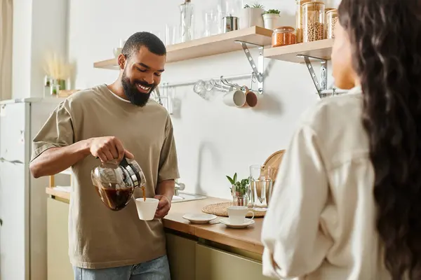 Un hombre vierte café para su pareja en su acogedora y cálida cocina llena de amor. - foto de stock