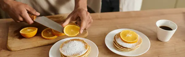 A man preps fresh orange slices while his partner eagerly awaits breakfast at home. — Stock Photo