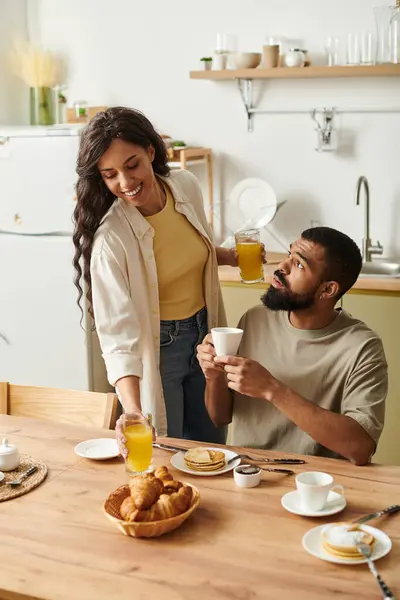 Una feliz pareja afroamericana comparte sonrisas sobre un desayuno relajado en casa. - foto de stock