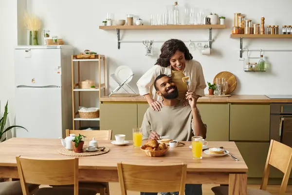 A couple enjoys a cozy breakfast at home, sharing laughter and affection in a warm atmosphere. — Stock Photo