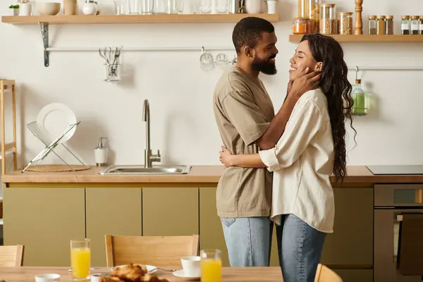 Um casal negro alegre compartilha um abraço amoroso em sua cozinha. — Fotografia de Stock