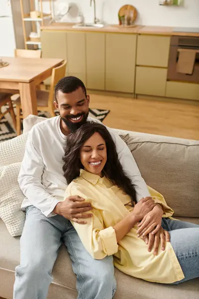 An affectionate African American couple shares joyful smiles while relaxing together on a sofa. — Stock Photo