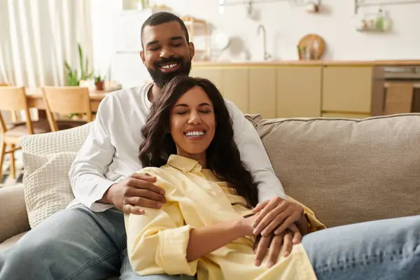 An African American couple sits on a couch, sharing smiles in their cozy home. — Stock Photo