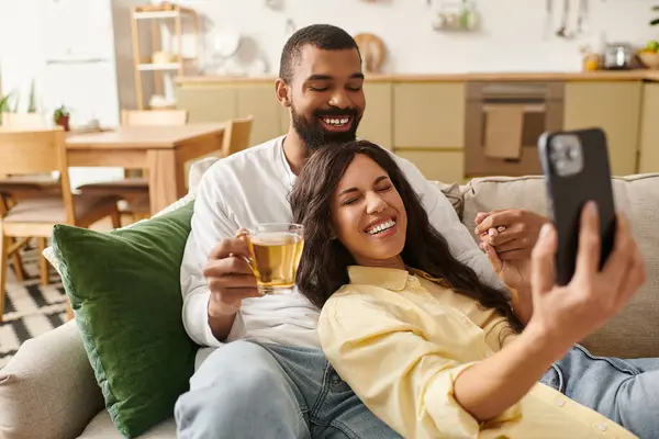 A happy couple shares laughter over warm drinks in their cozy home. — Stock Photo