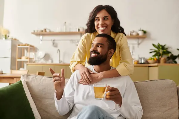 Eine Frau umarmt freudig ihren Partner, während er ein warmes Getränk in ihrem einladenden Wohnzimmer genießt. — Stockfoto