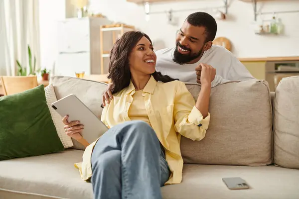 A happy African American couple relaxes at home, smiling and enjoying a tablet together. — Stock Photo