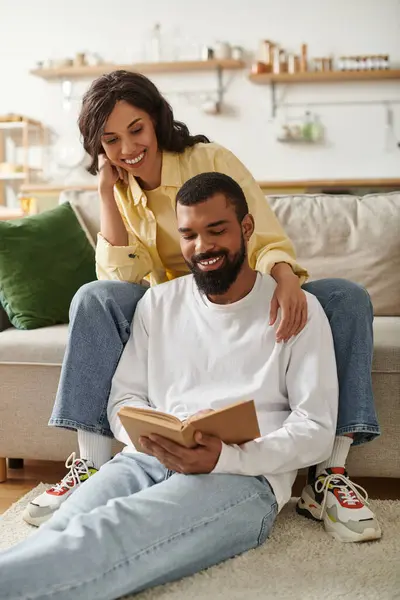 A man and woman enjoy quality time together at home, sharing smiles while reading a book. — Stock Photo