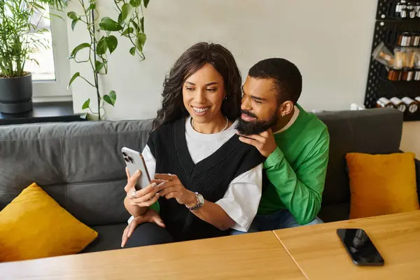 Una coppia felice condivide un momento intimo in un caffè, sorridendo mentre guardano il loro telefono insieme. — Foto stock