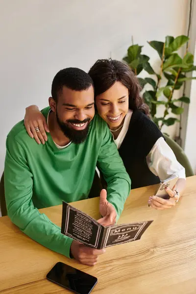 Una pareja afroamericana sonríe y comparte un momento alegre mientras mira el menú de la cafetería. - foto de stock