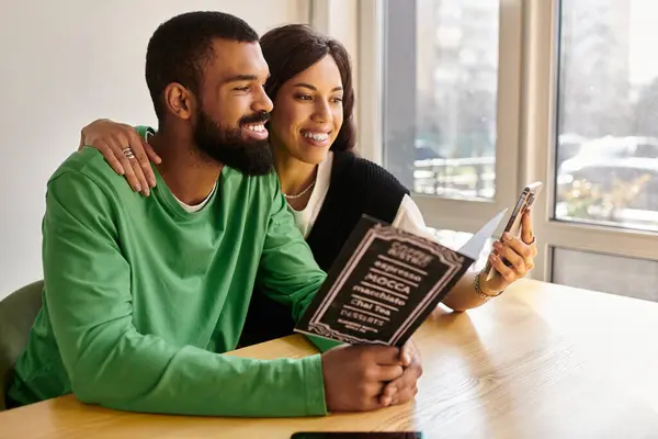 Um casal feliz gosta da companhia um do outro enquanto lê e usa seus telefones em um café acolhedor. — Fotografia de Stock