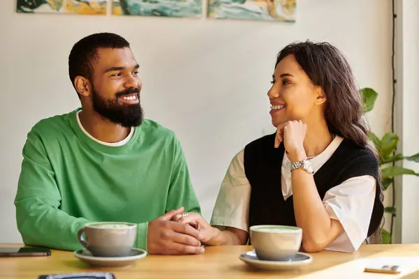 Una pareja afroamericana comparte sonrisas y bebidas calientes mientras está sentada cerca de una mesa de café. - foto de stock