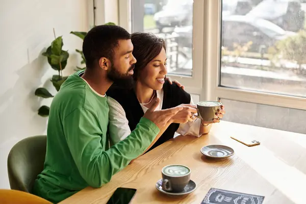 Una pareja afroamericana comparte risas y bebidas en un brillante café, disfrutando de un tiempo de calidad. - foto de stock