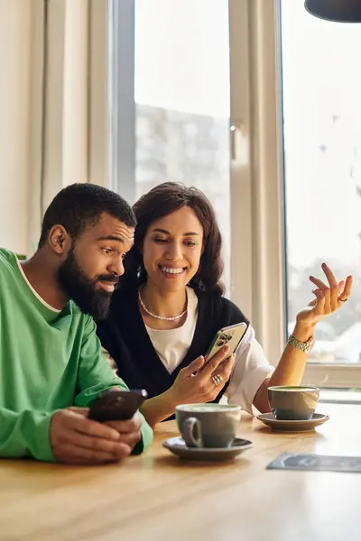 Una coppia afroamericana si rilassa insieme, sorseggiando caffè e usando i loro telefoni. — Foto stock