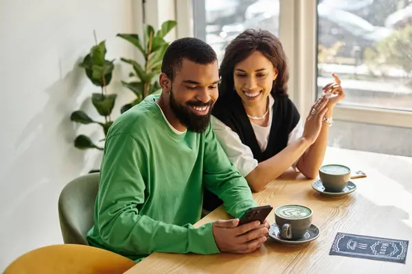 Zwei Leute entspannen sich und lächeln in einem Café, während sie an ihren Getränken nippen und auf ein Telefon schauen. — Stockfoto