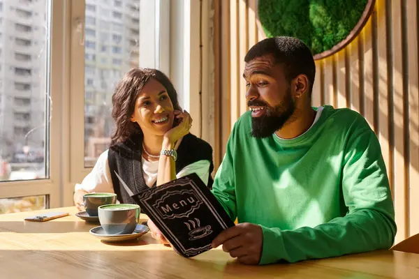 A couple enjoys each other's company while exploring a cafe menu in a warm and inviting atmosphere. — Stock Photo