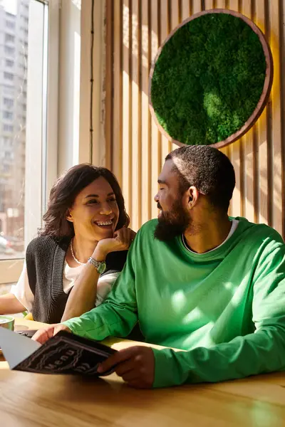 Una pareja disfruta de la compañía del otro, sonriendo y compartiendo un menú en un café con luz natural. - foto de stock