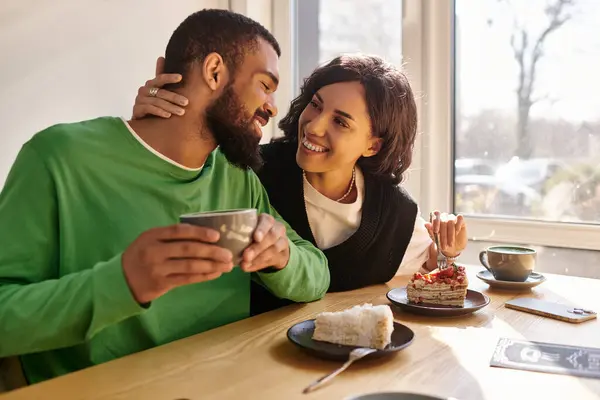 Couple aime les friandises sucrées et les boissons chaudes tout en partageant des sourires dans une atmosphère de café. — Photo de stock