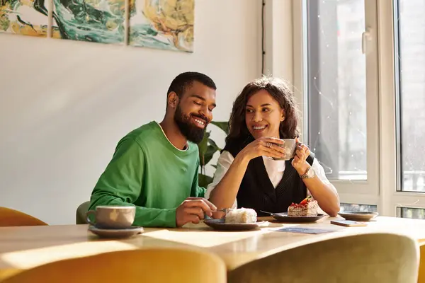 An African American couple enjoys coffee and dessert while sharing smiles in a cafe. — Stock Photo