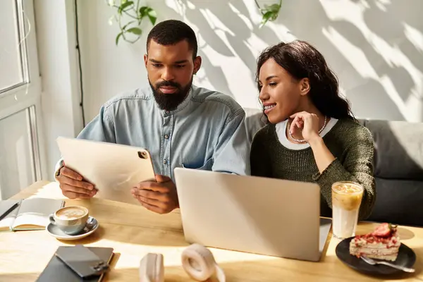 Dos freelancers afroamericanos comparten ideas sobre dispositivos en un vibrante café, inmersos en el trabajo. - foto de stock