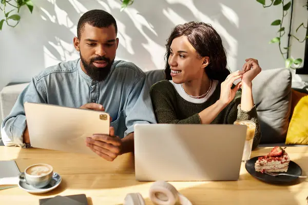 Una pareja afroamericana se dedica al trabajo remoto, compartiendo ideas y creatividad en un acogedor café. - foto de stock