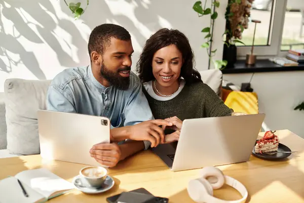 Pareja afroamericana se dedica a tareas de colaboración en sus dispositivos en un entorno de cafetería. - foto de stock