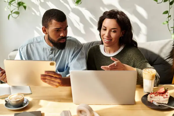 Una pareja afroamericana se dedica a un trabajo remoto, compartiendo ideas sobre computadoras portátiles en un café. - foto de stock