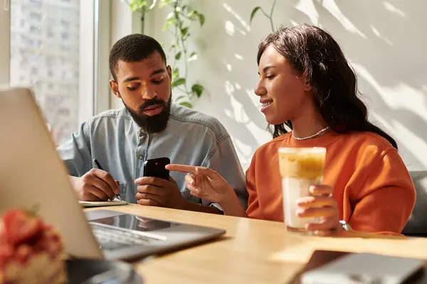 Pareja colabora en el trabajo freelance mientras disfruta de bebidas en un ambiente de cafetería amigable. - foto de stock