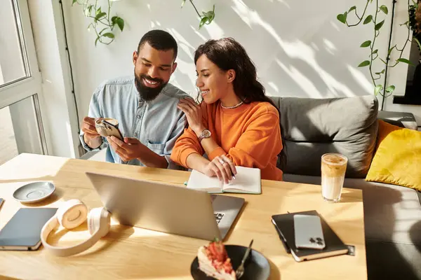 Una pareja afroamericana comparte ideas mientras trabajan remotamente en una vibrante atmósfera de cafetería. - foto de stock