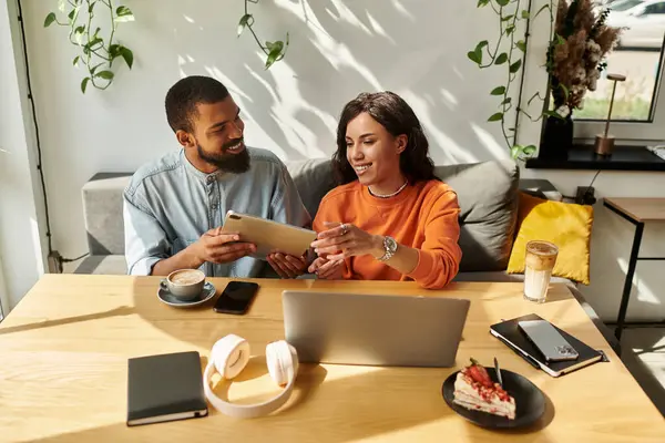 Una pareja afroamericana se dedica a un trabajo independiente remoto en un café, compartiendo ideas sobre el café. - foto de stock