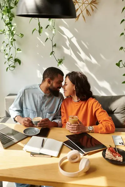 Pareja trabajando en computadoras portátiles mientras comparte bebidas y un postre en una cómoda cafetería. - foto de stock