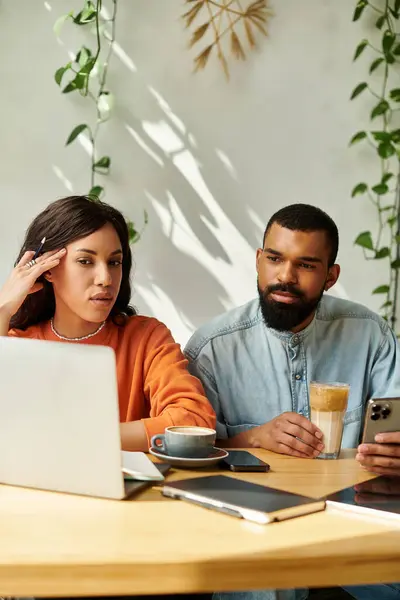 Pareja enfocada colabora en sus tareas freelance en un vibrante café mientras disfruta del café. - foto de stock
