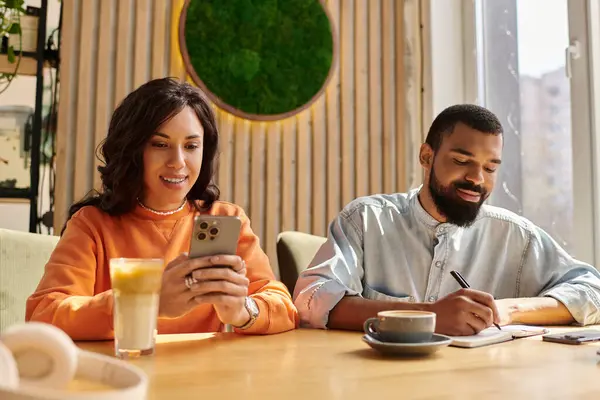 Una pareja afroamericana disfruta de un momento acogedor café, uno en un teléfono, la otra escritura. - foto de stock