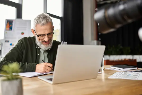 A focused individual writes notes while working on a laptop in a stylish office environment — Stock Photo