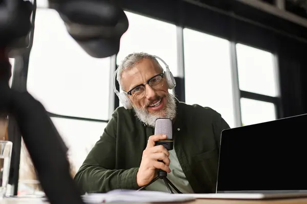 A man with glasses and headphones passionately talks into a microphone at his desk. — Stock Photo