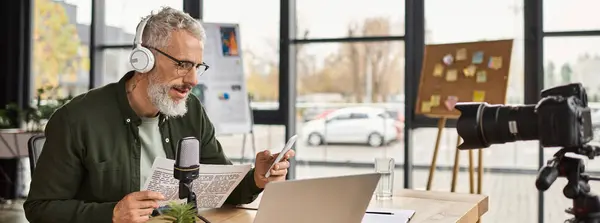 A man with glasses and headphones discusses ideas while using a laptop in a bright office. — Stock Photo