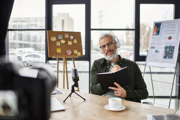 Business professional with headphones brainstorms, takes notes, and sips coffee. — Stock Photo