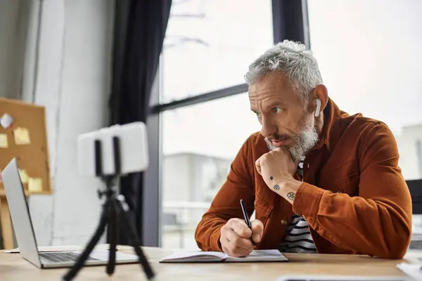 Un professionista in un ufficio accogliente prende appunti durante una riunione online, pienamente impegnato. — Foto stock